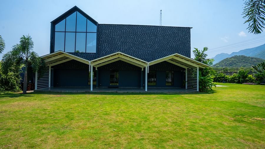 Love Letter at Darza Resort featuring a modern, dark-coloured building with large windows and covered porches sits on a bright green lawn under a clear, sunny sky.