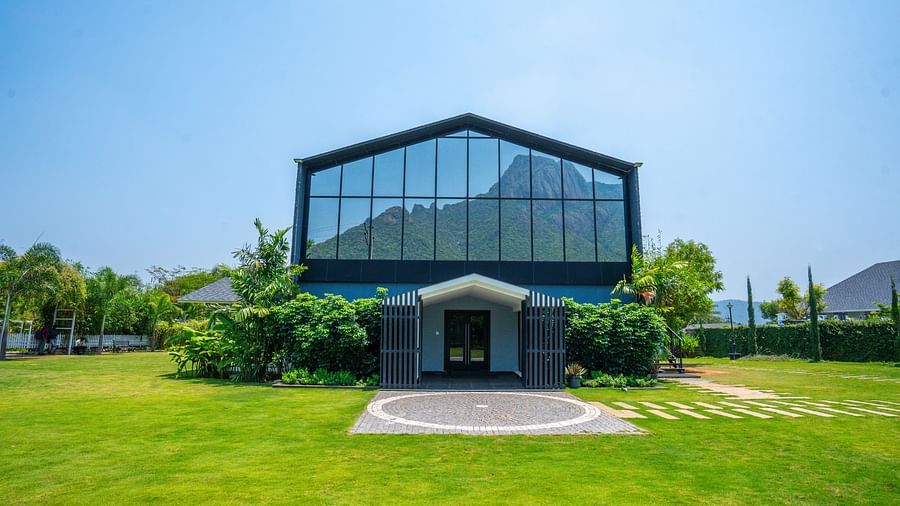 Entrance of Love Letter at Darza Resort with large glass windows reflecting the sky stands on a vibrant green lawn surrounded by greenery.