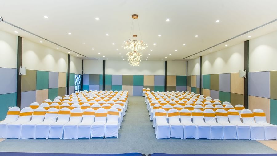 A well-lit Royal Affair at Darza Resort is arranged with numerous white chairs decorated with orange sashes, set up for an audience facing a stage area.