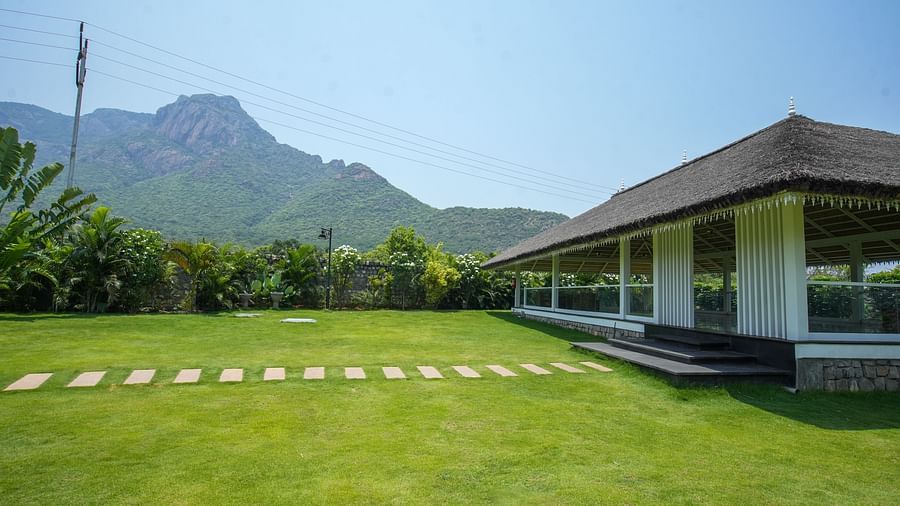 Slice of Heaven at Darza Resort featuring a bright green lawn with a stone pathway leads to a white building with a thatched roof, set against a backdrop of lush greenery and mountains.