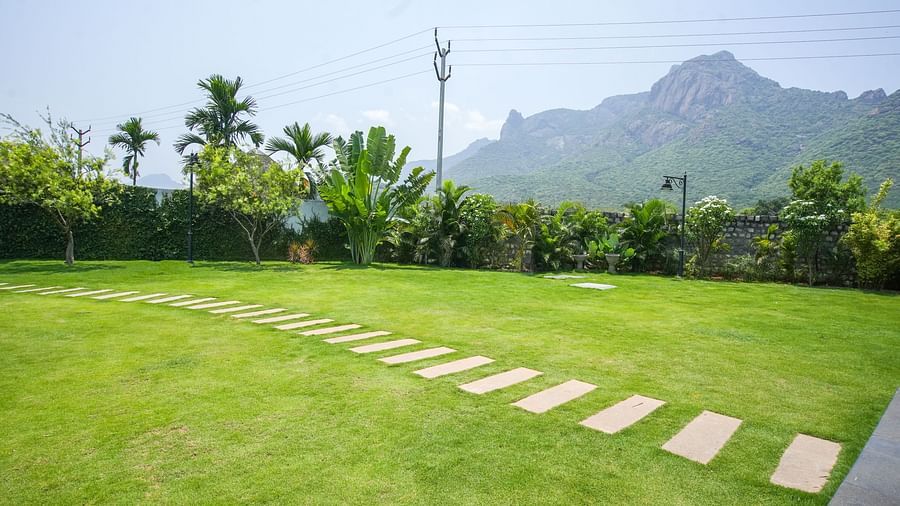 Slice of Heaven at Darza Resort featuring a lush green lawn with a stone pathway stretches towards verdant trees and a majestic mountain range under a bright, clear sky.