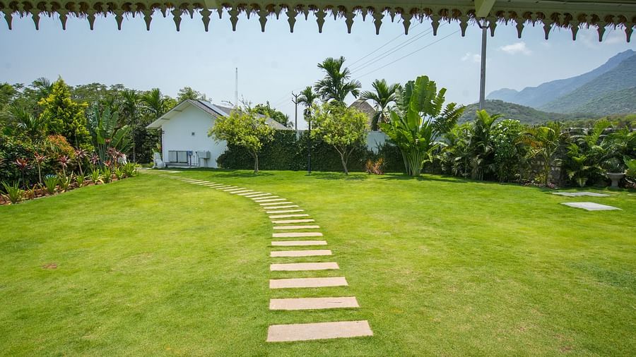 Slice of Heaven at Darza Resort featuring a stone pathway winding through a lush green lawn, leading towards white buildings and tropical foliage under a bright, clear sky.