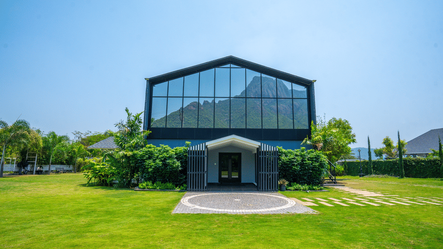 Entrance of Love Letter event venue at Darza Resort with large glass windows reflecting the sky stands on a vibrant lawn surrounded by greenery