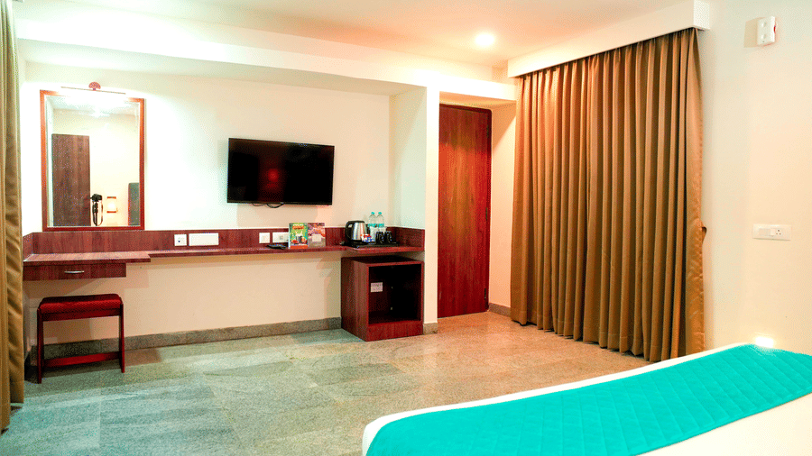A bedroom with a bed, a television, a desk, and curtains at DNC Shevaroys Resorts and Spa.