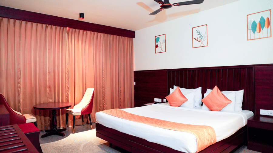 A bedroom with a bed, curtains, and framed wall art at DNC Shevaroys Resorts and Spa.