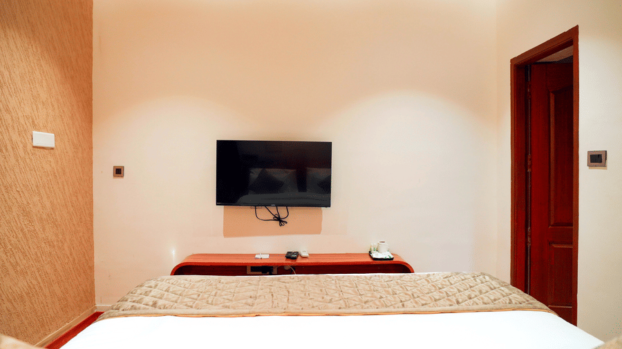 A bedroom with a bed, a television, and 2 doorways at DNC Shevaroys Resorts and Spa.