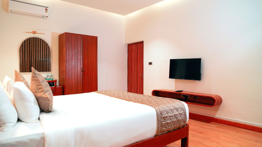 A bedroom with a bed, a wardrobe, and a television at DNC Shevaroys Resorts and Spa.