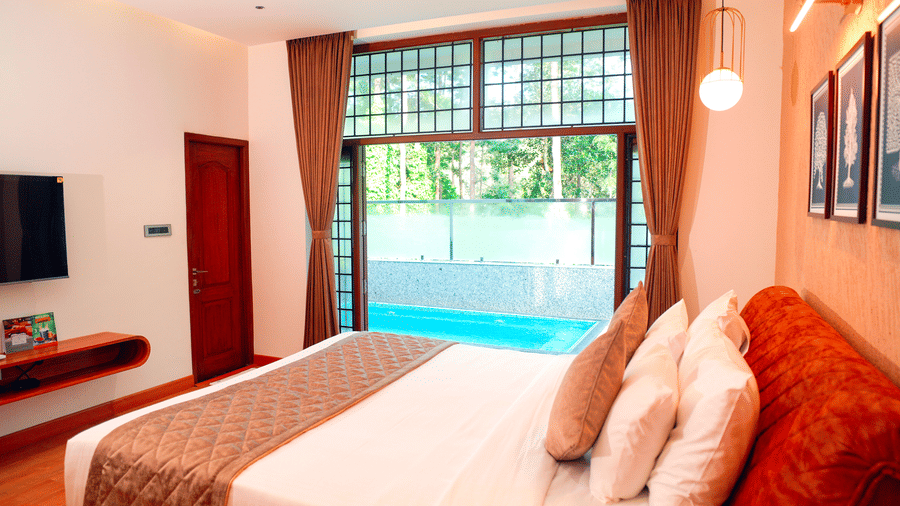 A bedroom with a bed, a television, and a view of a pool at DNC Shevaroys Resorts and Spa.