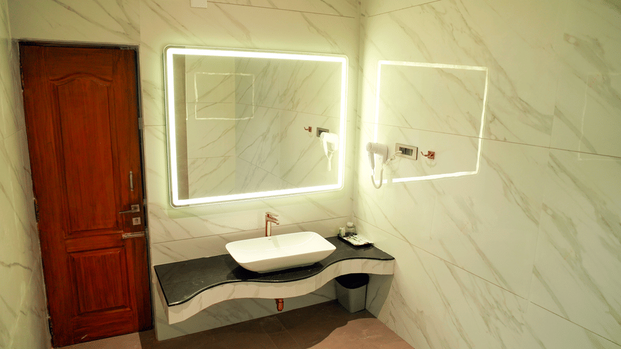 A bathroom with a sink, a mirror, and a door at DNC Shevaroys Resorts and Spa.