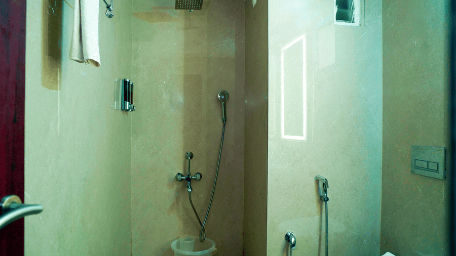 A bathroom view shows a shower area, a toilet, a bucket, and a mirror at DNC Shevaroys Resorts and Spa.