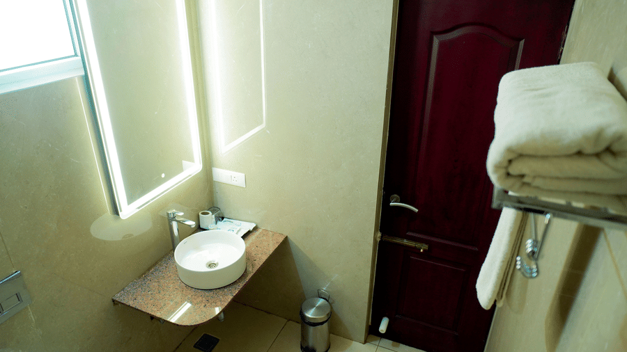 A bathroom view shows a basin, a mirror, a shelf with towels, and a door at DNC Shevaroys Resorts and Spa.