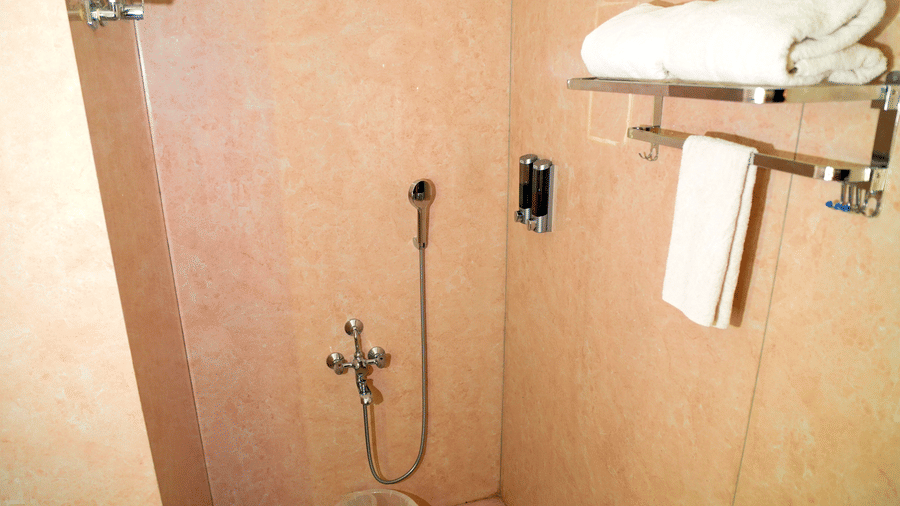 A bathroom shower area with a showerhead, a bucket, and shelves at DNC Shevaroys Resorts and Spa.