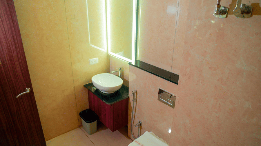 A bathroom with a sink, a mirror, a toilet, and a door at DNC Shevaroys Resorts and Spa.