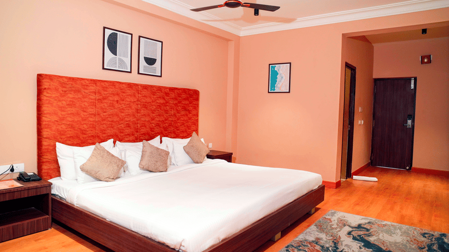 A bedroom with a bed, chairs, and framed wall art at DNC Shevaroys Resorts and Spa.