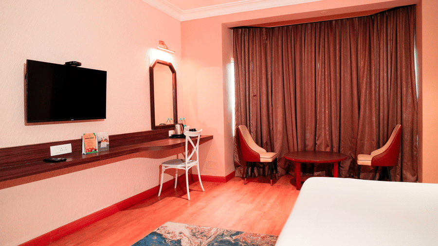 A bedroom with a bed, a wall-mounted television, and chairs at DNC Shevaroys Resorts and Spa.