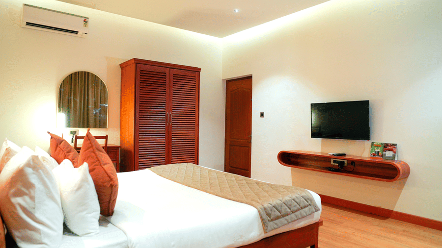 A bedroom with a bed, a wardrobe, and a television at DNC Shevaroys Resorts and Spa.