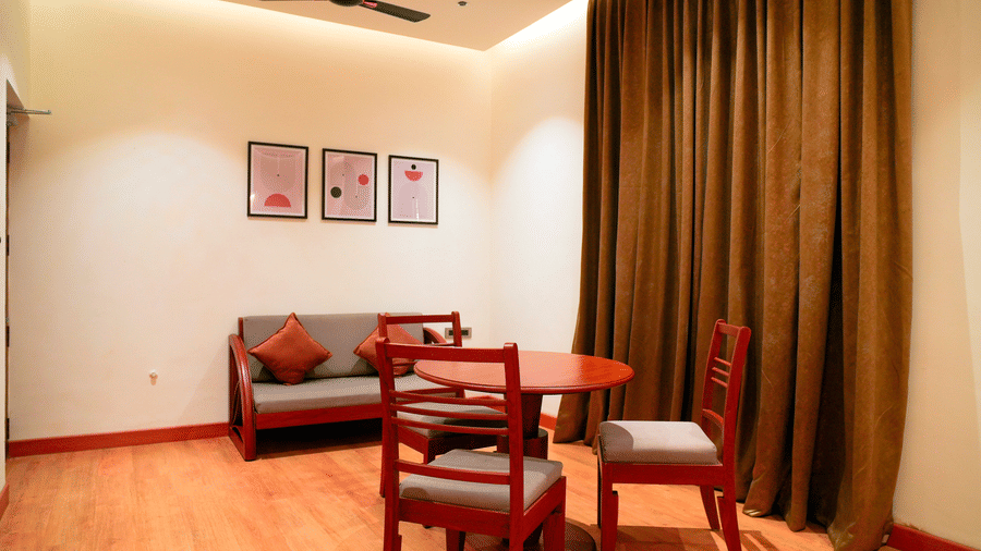 A seating area with a table, chairs, and framed wall art at DNC Shevaroys Resorts and Spa.