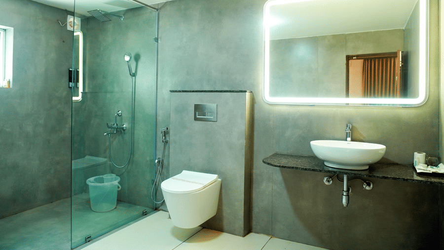 A bathroom with a shower area, a toilet, a sink, and a mirror at DNC Shevaroys Resorts and Spa.