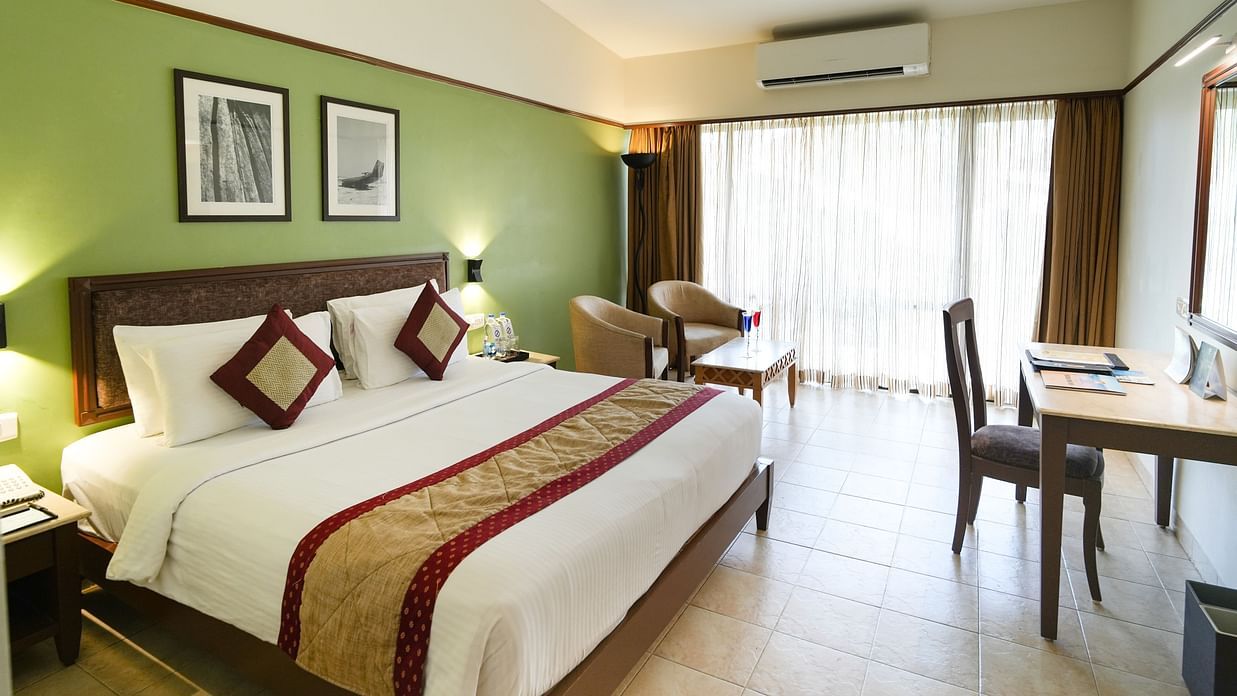 A well-lit modern bedroom with bright interiors and a warm atmosphere, featuring a table, chair, portraits on the wall and air conditioner