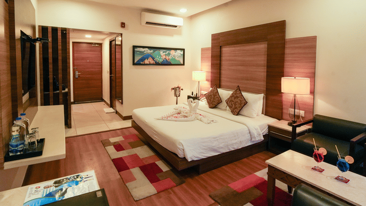 Hotel room with a modern interior, featuring a king size bed, decorative pillows, bedside lamps, a seating area with drinks, a wall-mounted TV, and wooden accents - MGM Beach Resorts
