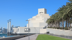 The Museum of Islamic Art in Doha, Qatar, is a white stepped building with a small tower, surrounded by green lawns, palm trees, and a waterfront promenade.