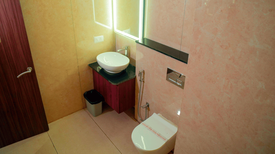 A bathroom with a sink, a mirror, a toilet, and a door at DNC Shevaroys Resorts and Spa.