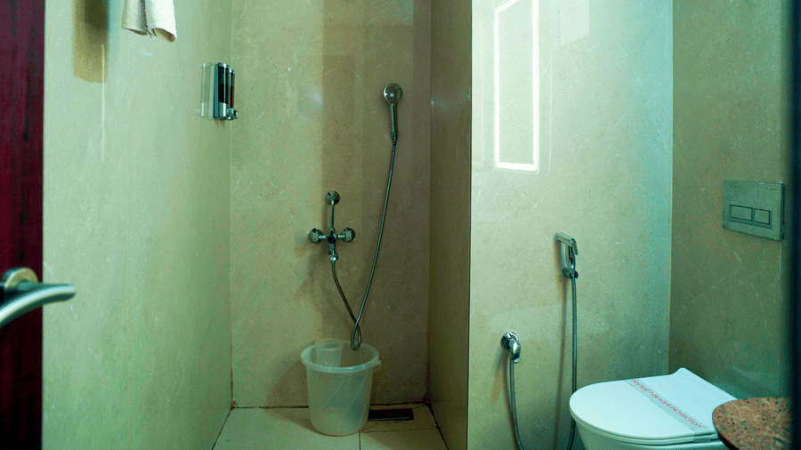 A bathroom view shows a shower area, a toilet, a bucket, and a mirror at DNC Shevaroys Resorts and Spa.