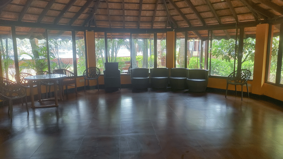 Large circular hall with wooden roof, glass windows, and seating at Paradise Lagoon Resort, Udupi.