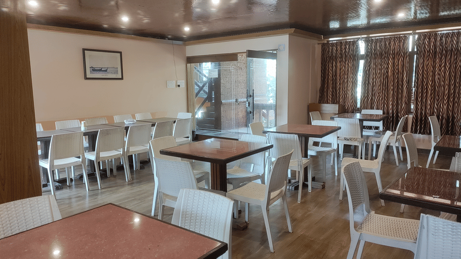Indoor dining area with tables and white chairs arranged neatly at Paradise Lagoon Resort, Udupi.