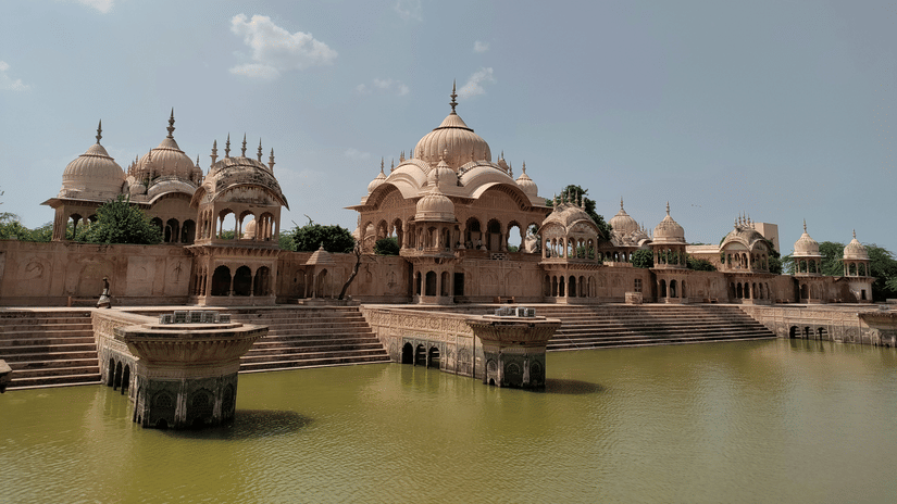 Large, ancient stone temple complex reflected in a still body of water under a bright sky.