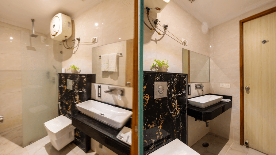 Bathroom featuring a dark marble feature wall behind a wall-mounted toilet, a modern vanity unit, and a glass-enclosed shower area with warm accent lighting at Hotel Corporate Suites