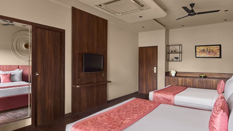 Super Deluxe Family Room featuring two beds with pink runners, wooden wall panels, a mounted TV, and an adjoining room at DGV Resort by Treat, Silvassa.