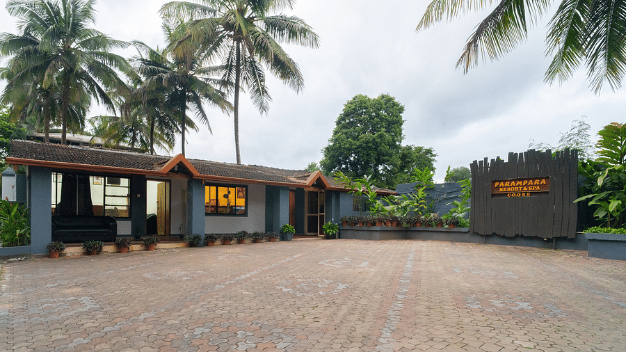 Facade of Parampara Resort & Spa, Kushalnagar with a large open space in front and trees surrounding it.