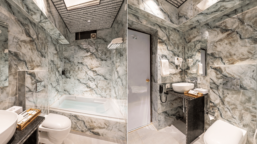 Luxurious hotel bathroom with natural stone wall cladding, a glass shower partition, a deep bathtub, and modern fixtures.