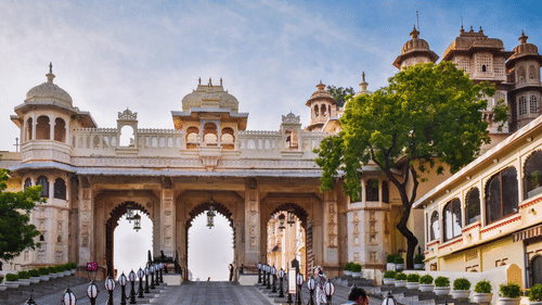 Ornate palace entrance with three large arches, surrounded by elegant architecture and lush greenery under a clear sky.
