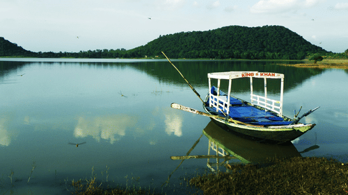 A boat present on a Lake with lush green and clear blue sky in the landscape.