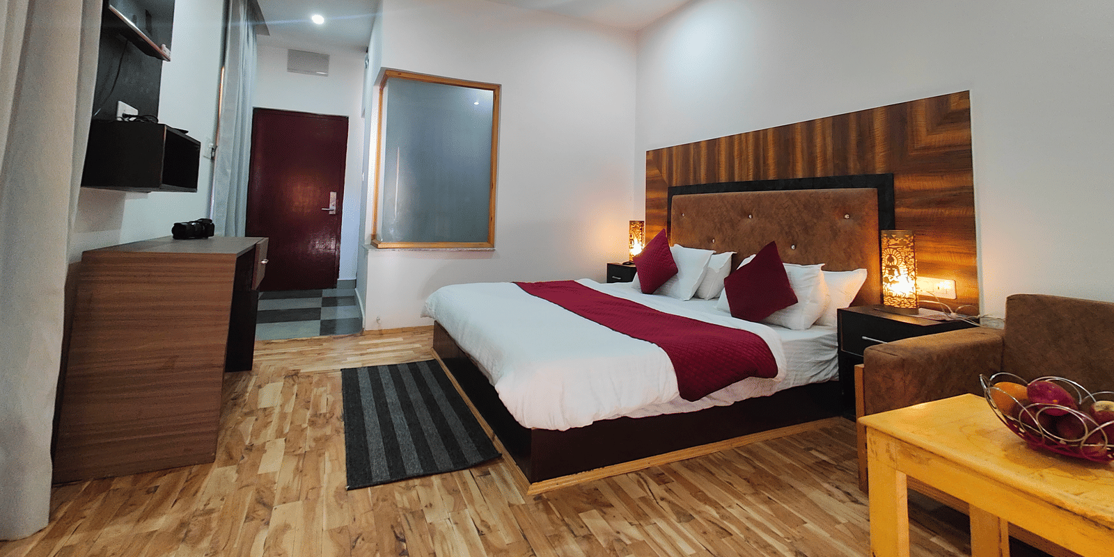 A well-furnished guest room with wooden flooring, a large bed, and warm lighting at Indus Serenity Retreat.