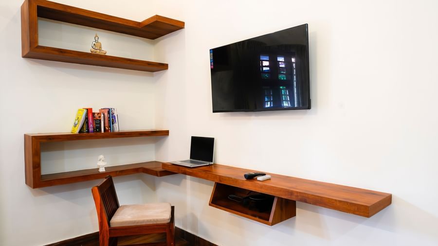A different perspective of the unique floating wooden desk and shelves in the villa at Bhuthanakadu Retreat, with a TV mounted on the wall above the work area.