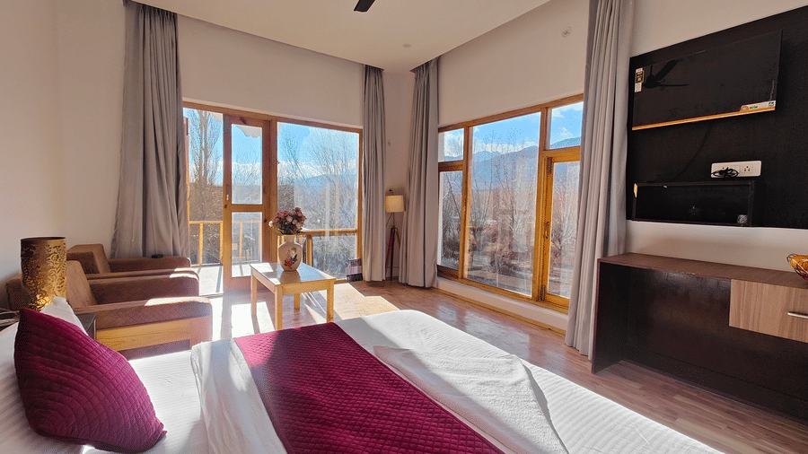 A bright hotel bedroom with large windows offering views of the surrounding mountains at Indus Serenity Retreat.