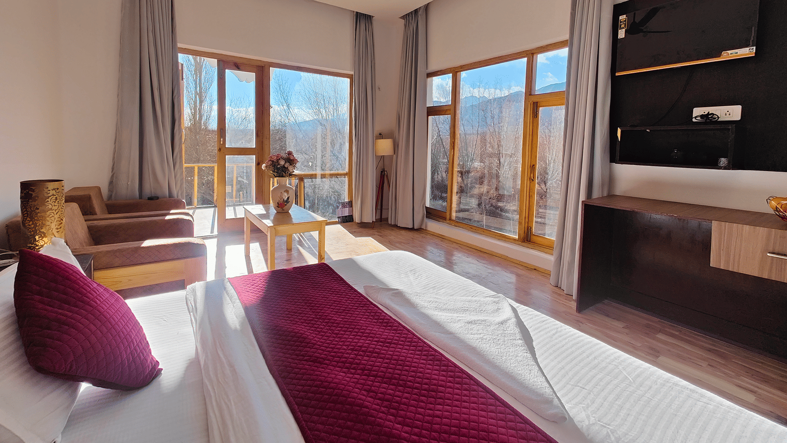 A bright hotel bedroom with large windows offering views of the surrounding mountains at Indus Serenity Retreat.