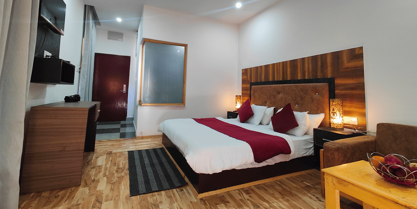 A well-furnished guest room with wooden flooring, a large bed, and warm lighting at Indus Serenity Retreat.