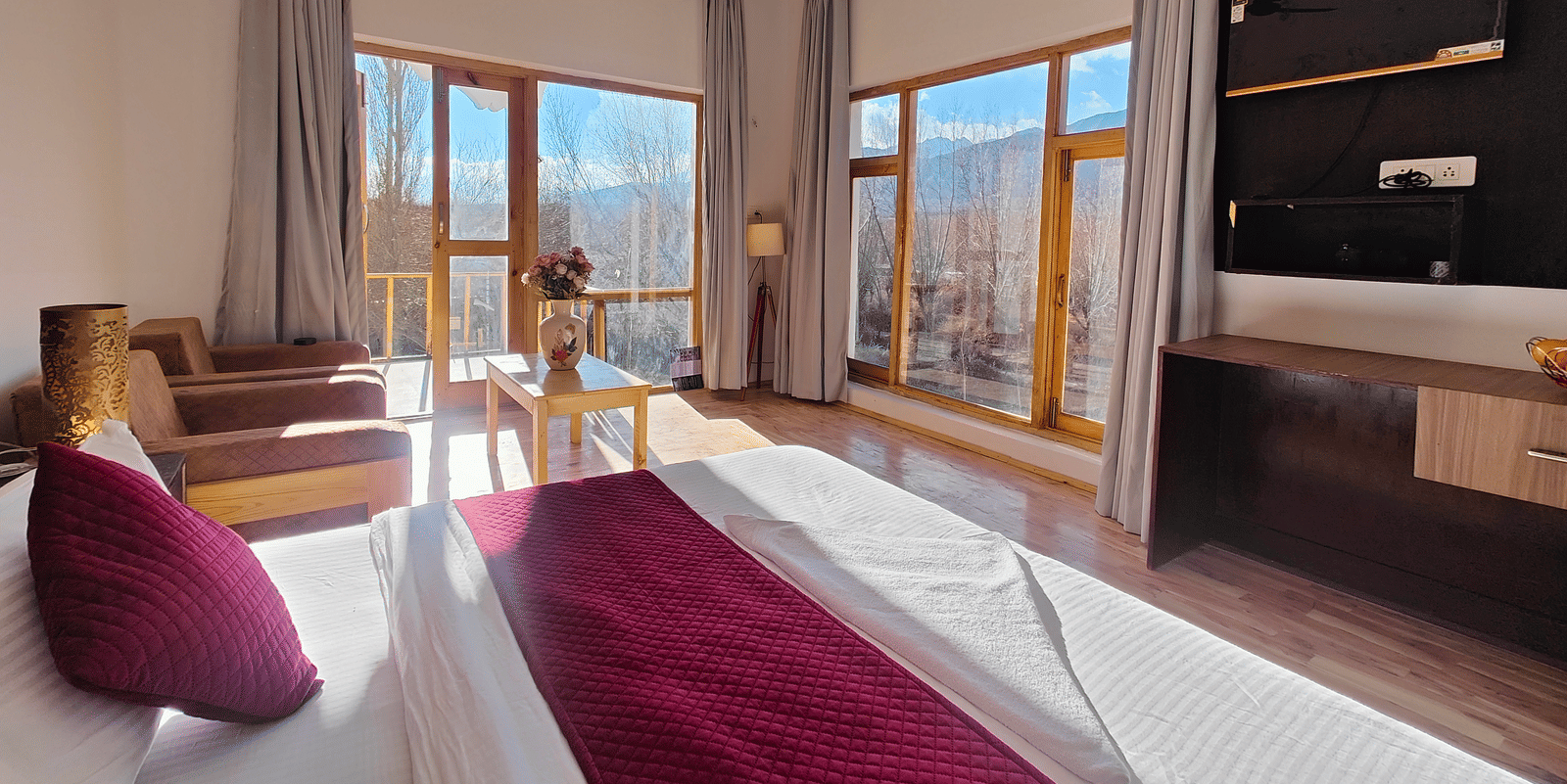 A bright hotel bedroom with large windows offering views of the surrounding mountains at Indus Serenity Retreat.