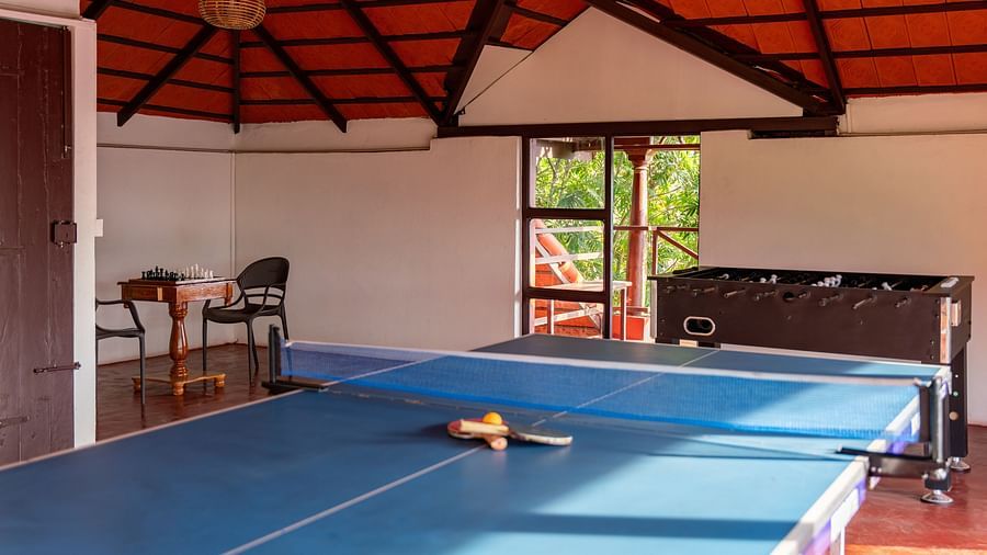 Game room with a ping pong table and foosball, featuring wooden ceiling and ample natural light. | Mango Hill, Yercaud