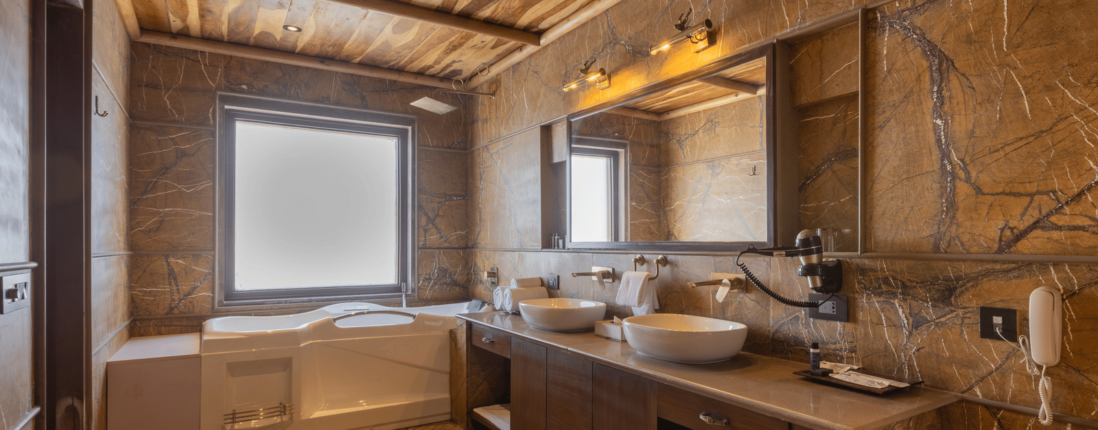 A luxurious bathroom at Aamaghati Wildlife Resort with twin sinks, stone walls, and large mirrors creating a stylish and functional space.