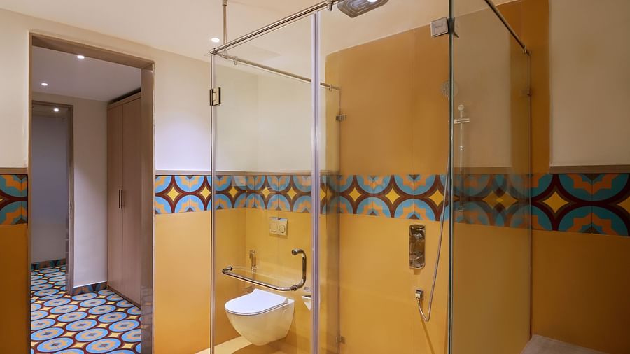 Modern bathroom with a glass-enclosed shower, wall-mounted toilet, and vibrant yellow walls accented by colourful patterned tiles - Voyage The Solitaire Bliss.