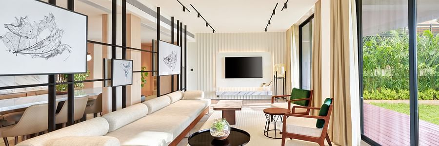 A long sofa with a tv wall mounted in the background and a floor to ceiling window opposite the sofa inside the Presidential Suite - The Resort, Mumbai