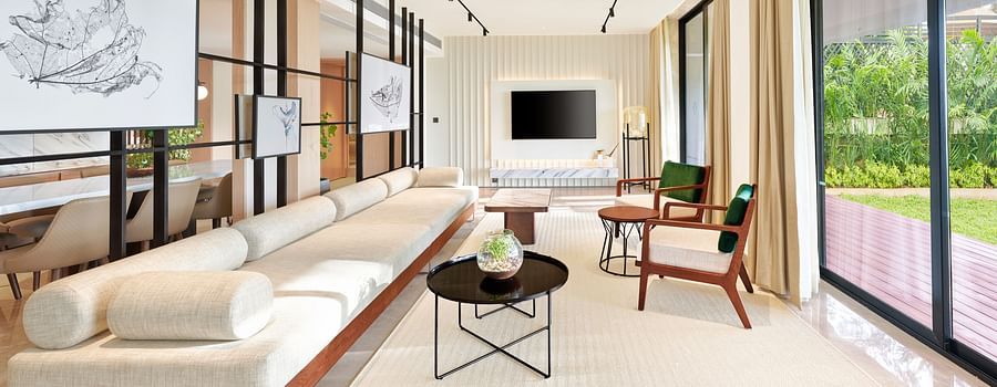 A long sofa with a tv wall mounted in the background and a floor to ceiling window opposite the sofa inside the Presidential Suite - The Resort, Mumbai