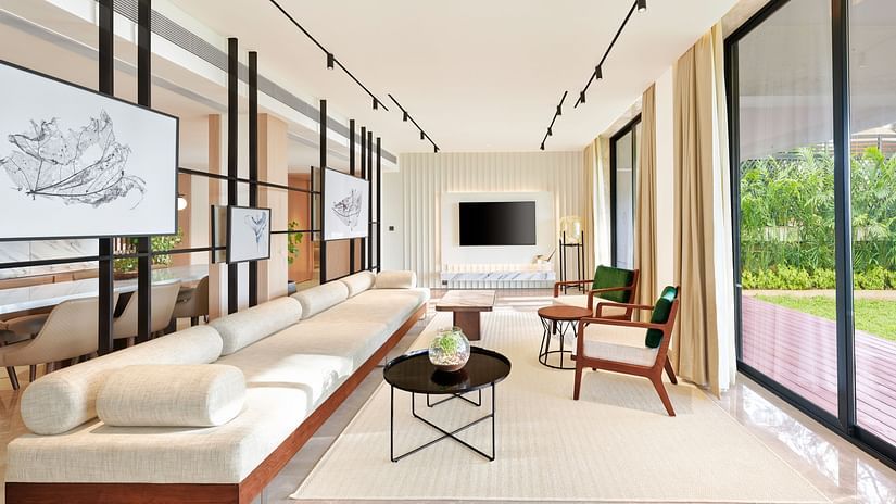 A long sofa with a tv wall mounted in the background and a floor to ceiling window opposite the sofa inside the Presidential Suite - The Resort, Mumbai