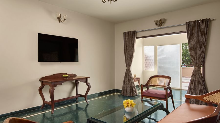 A well-furnished living room of Signature Suite with a wall-mounted TV, wooden furniture, and a outdoor view at DGV Resort by Treat, Silvassa.