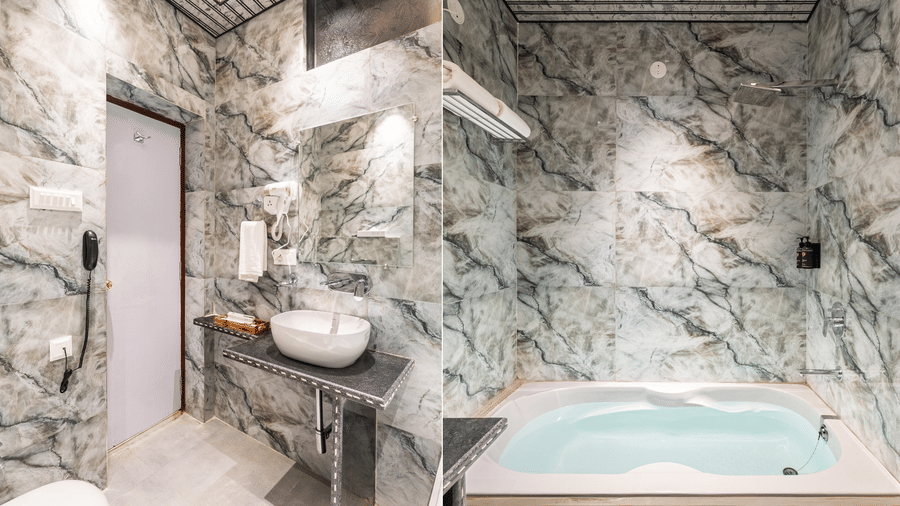Luxurious hotel bathroom with grey marble wall, freestanding wash basin, toilet, and a large jacuzzi bath/hot tub.